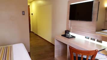 A hotel room with a wooden desk, a flat-screen TV, a chair, and a bed with striped bedding.