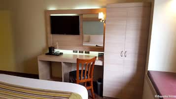 Een hotelkamer met een bed, bureau met een computer, een stoel en een garderobe.