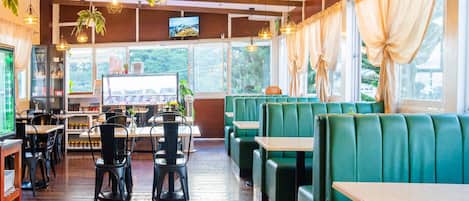 A restaurant interior with wooden floors, green booths, and hanging pendant lights.
