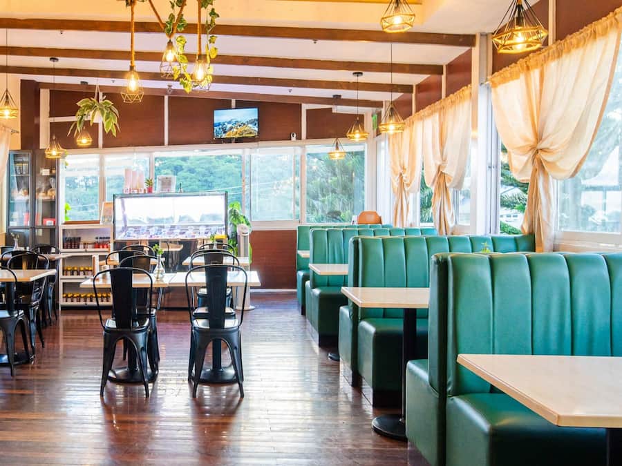 Interior de restaurante con pisos de madera, asientos tipo banca verdes y lámparas colgantes.