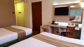 A hotel room with two beds, a desk with a chair, a mirror, and a television.