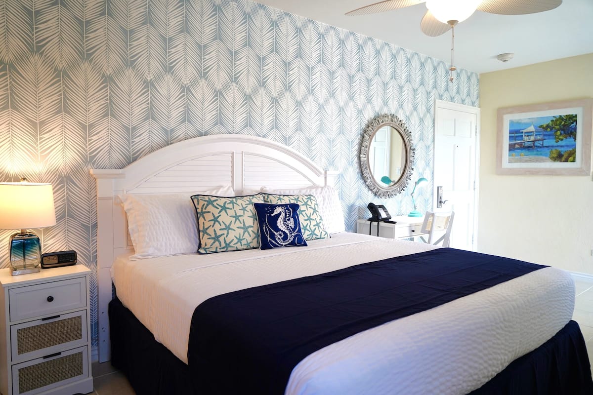 A neatly made bed with a white headboard, a blue and white patterned wall, and a framed picture on the wall.