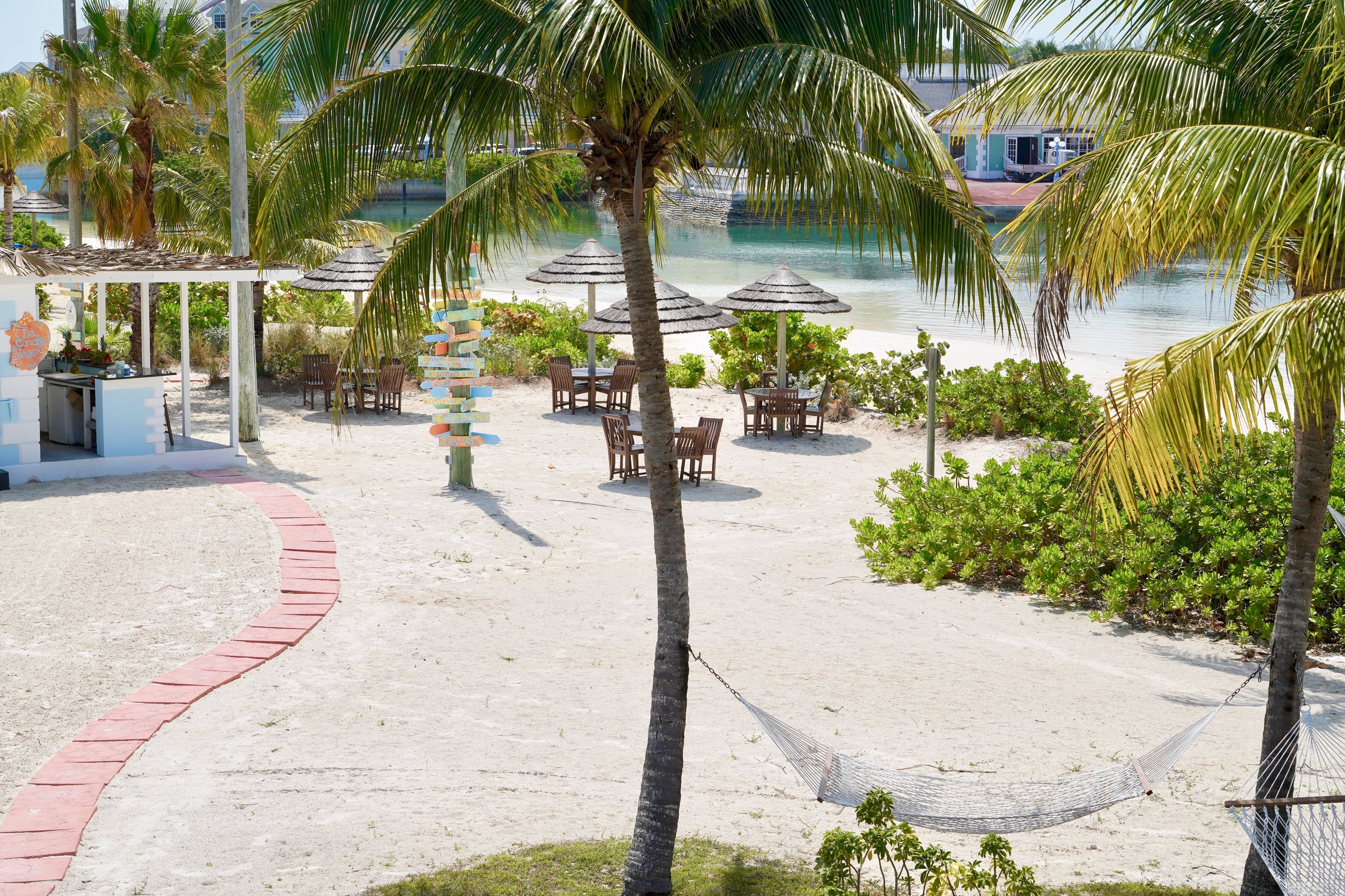 Un resort frente a la playa con piscina, mobiliario exterior y palmeras.