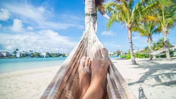 A hammock on a beach with a clear sky and palm trees.