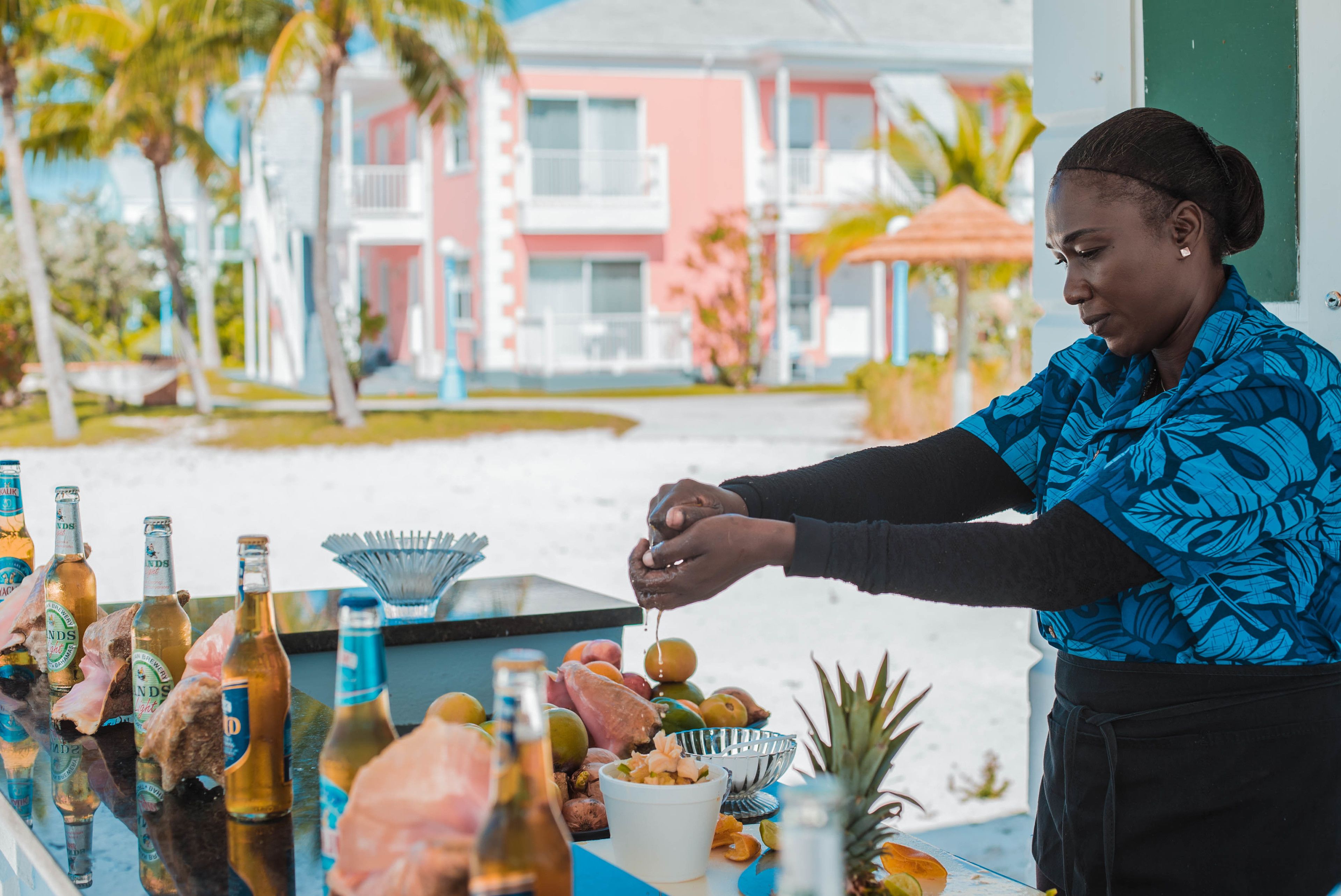 A person preparing food at an outdoor bar with a view of a colorful building and palm trees.