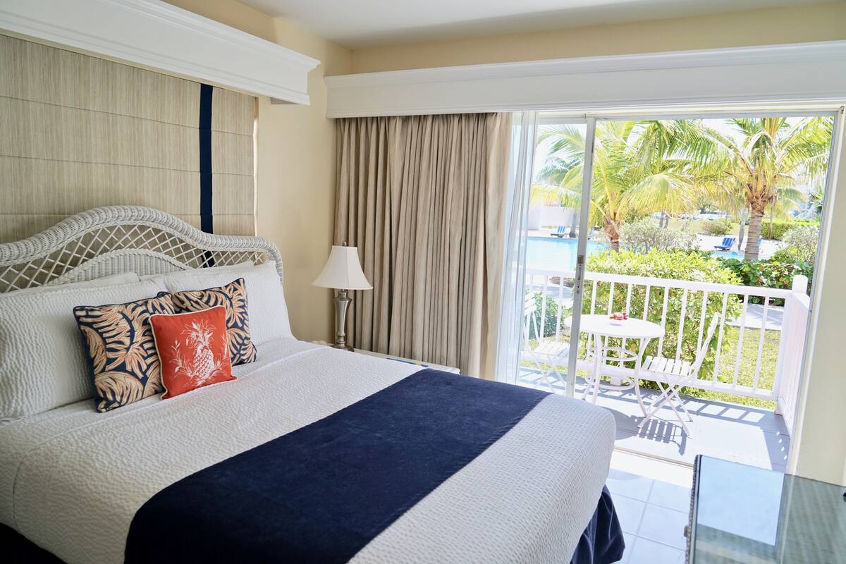 A hotel room with a large bed, a view of a pool and palm trees through a sliding glass door.