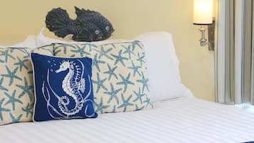 Una cama con ropa blanca, un cojín con forma de caballito de mar azul y un adorno de pez en la cabecera.