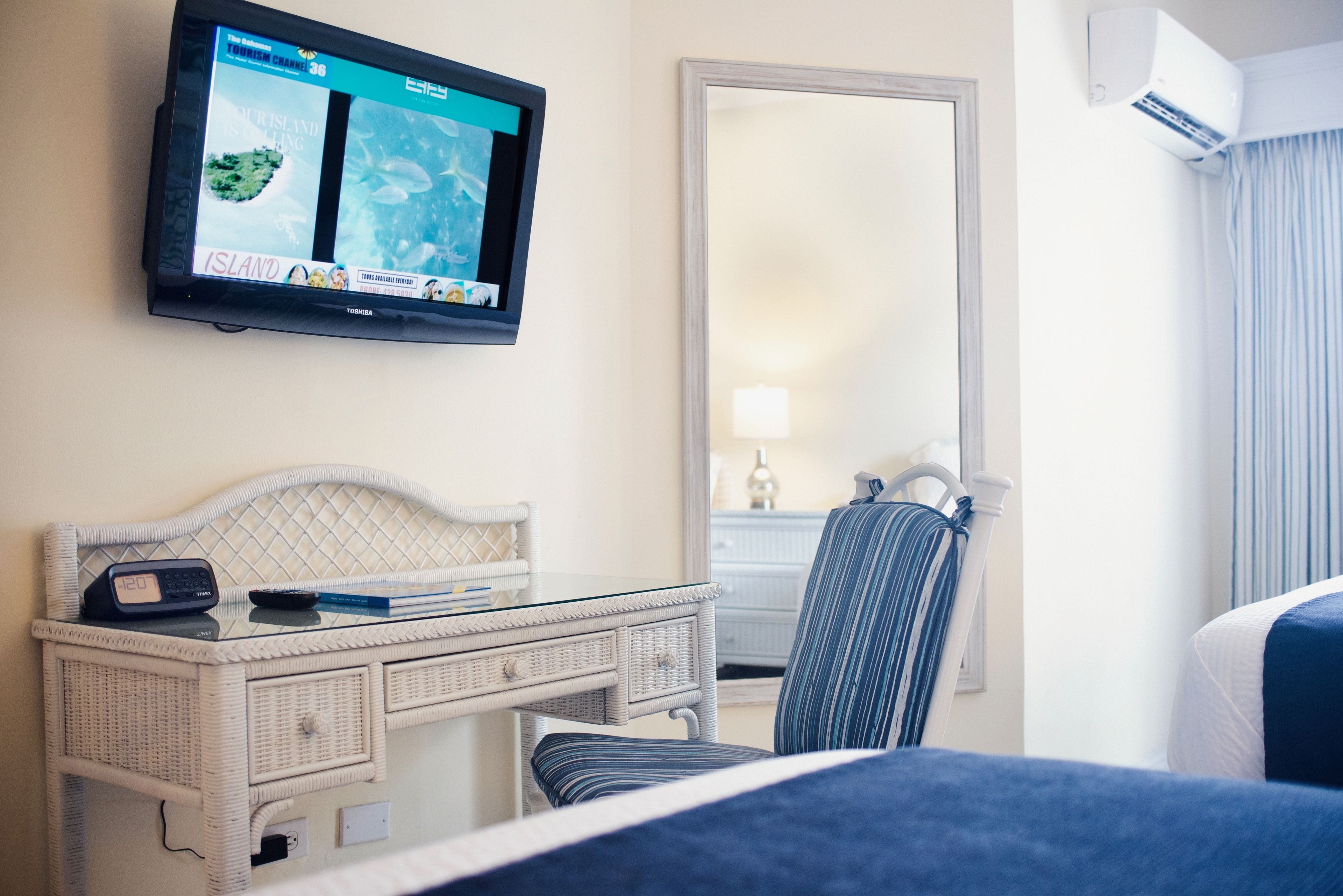 A hotel room with a bed, a desk with a TV, a chair, and a mirror.