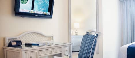 A hotel room with a bed, a desk with a TV, a chair, and a mirror.