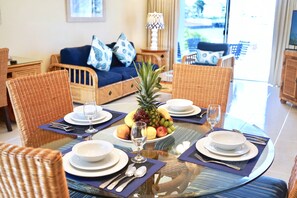 A dining area with wicker chairs, a glass table, and a fruit bowl.