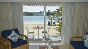 Una habitación con vista a la playa, dos sofás de mimbre con cojines, una mesita con un cuenco y una copa, y una zona de patio con sillas y una mesa.