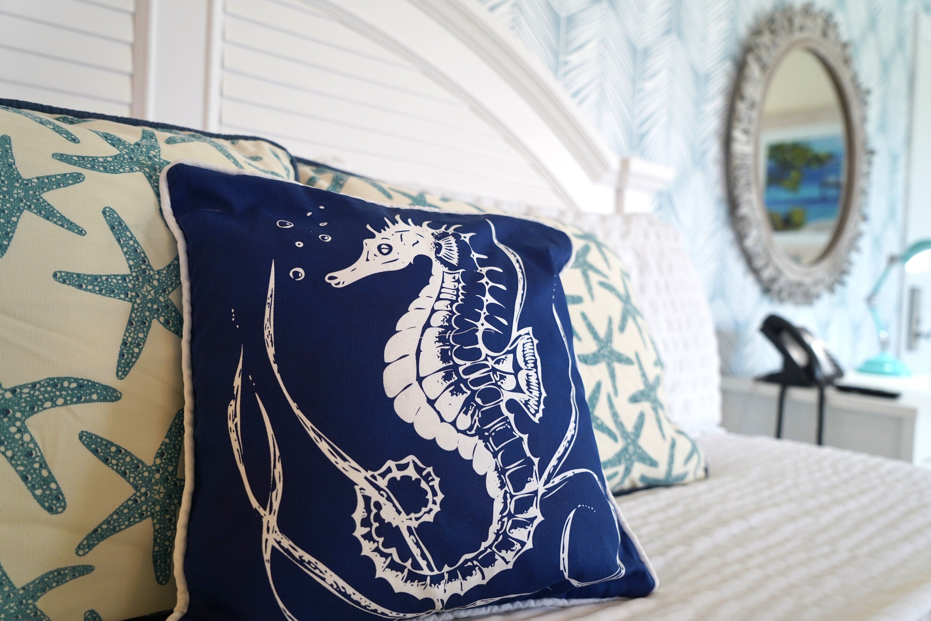 A bed with a white headboard, a blue and white seahorse pillow, and a starfish pattern pillow.