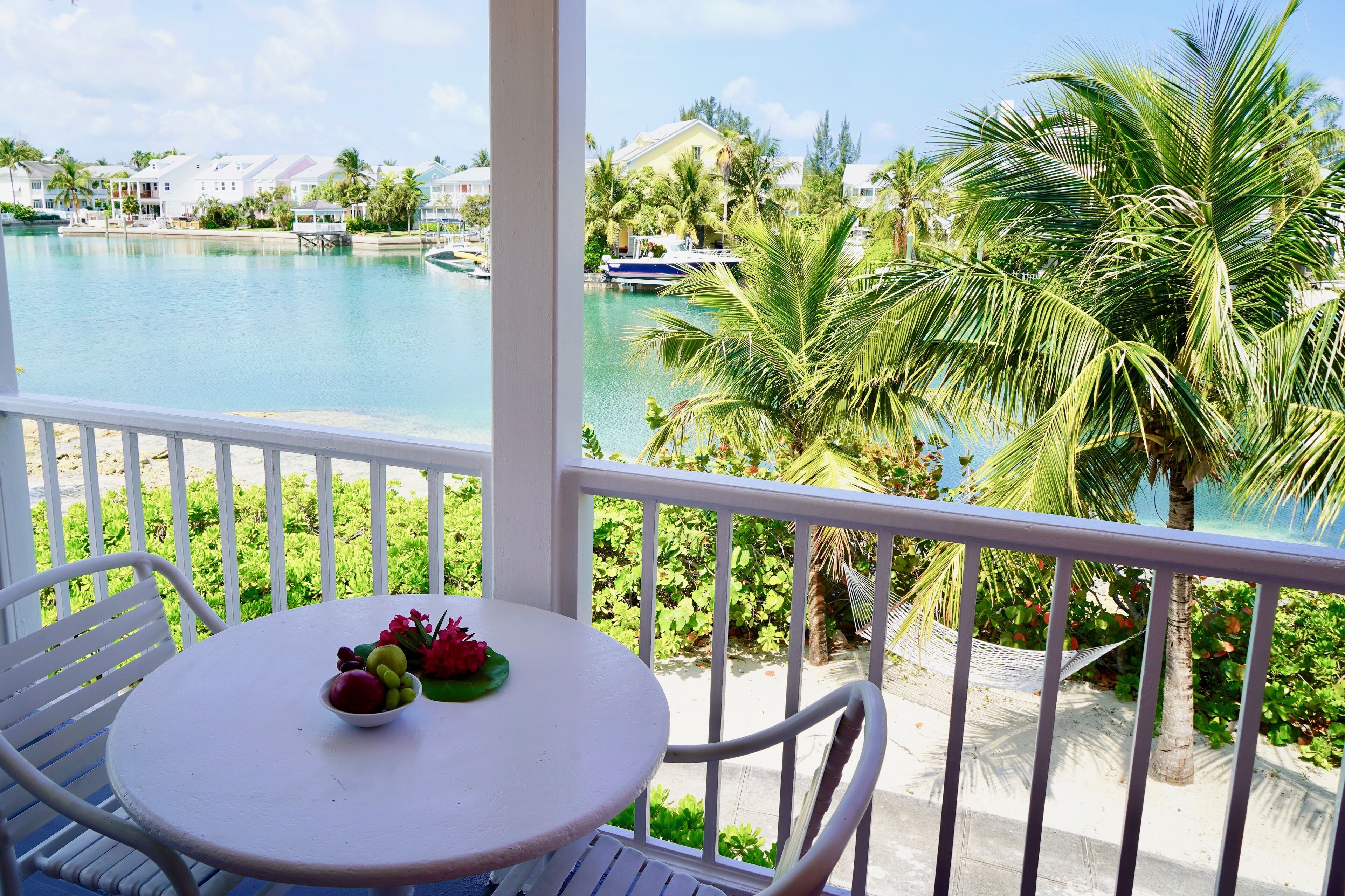 A balcony with a view of a swimming pool, palm trees, and a boat.