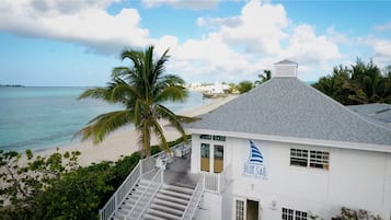 Un edificio blanco con un letrero que dice "BLUE SAIL Restaurant Bar" cerca de una playa con palmeras y el océano.