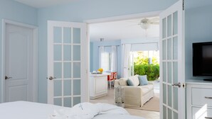 A hotel room with a bed, a TV, a dining area, and a view of the outdoors. - Beach House - Adults Only (Providenciales)