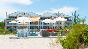 A beachfront hotel with multiple balconies, outdoor seating, and umbrellas. - Beach House - Adults Only (Providenciales)
