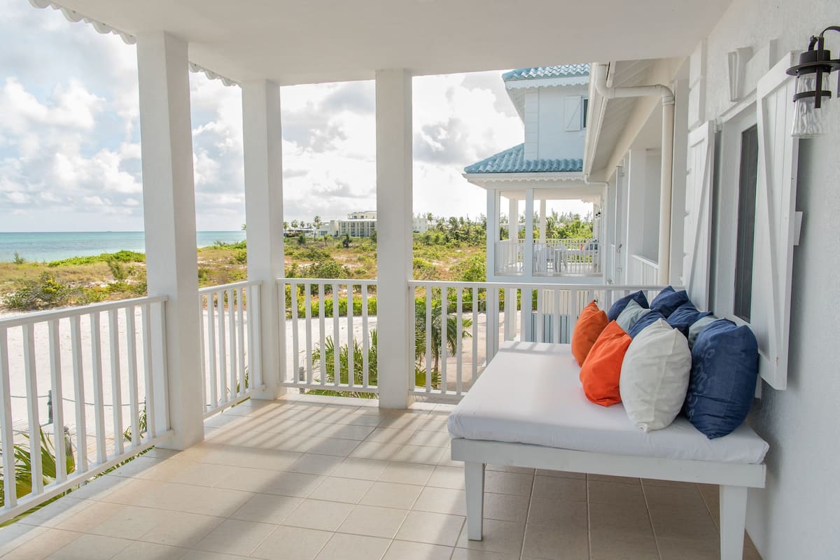 Ein überdachter Balkon mit einer weißen Bank und bunten Kissen, mit Blick auf einen Strand und Gebäude.