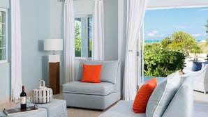 A modern room with a light blue sofa, a small table with a bottle and glasses, and a view of the ocean through large windows. - Beach House - Adults Only (Providenciales)