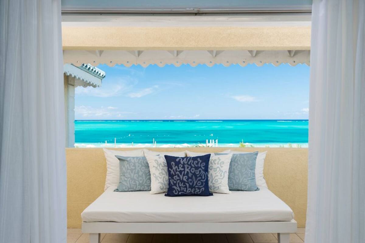 Ein Bett mit Blick auf den Ozean, einem weißen Moskitonetz und gemusterten Kissen.