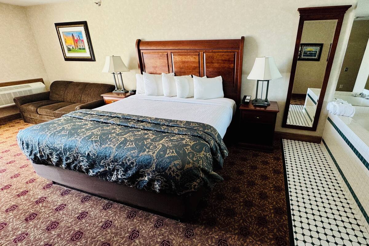 A hotel room with a large bed, a sitting area with a sofa, a bathroom with a bathtub, and a mirror.