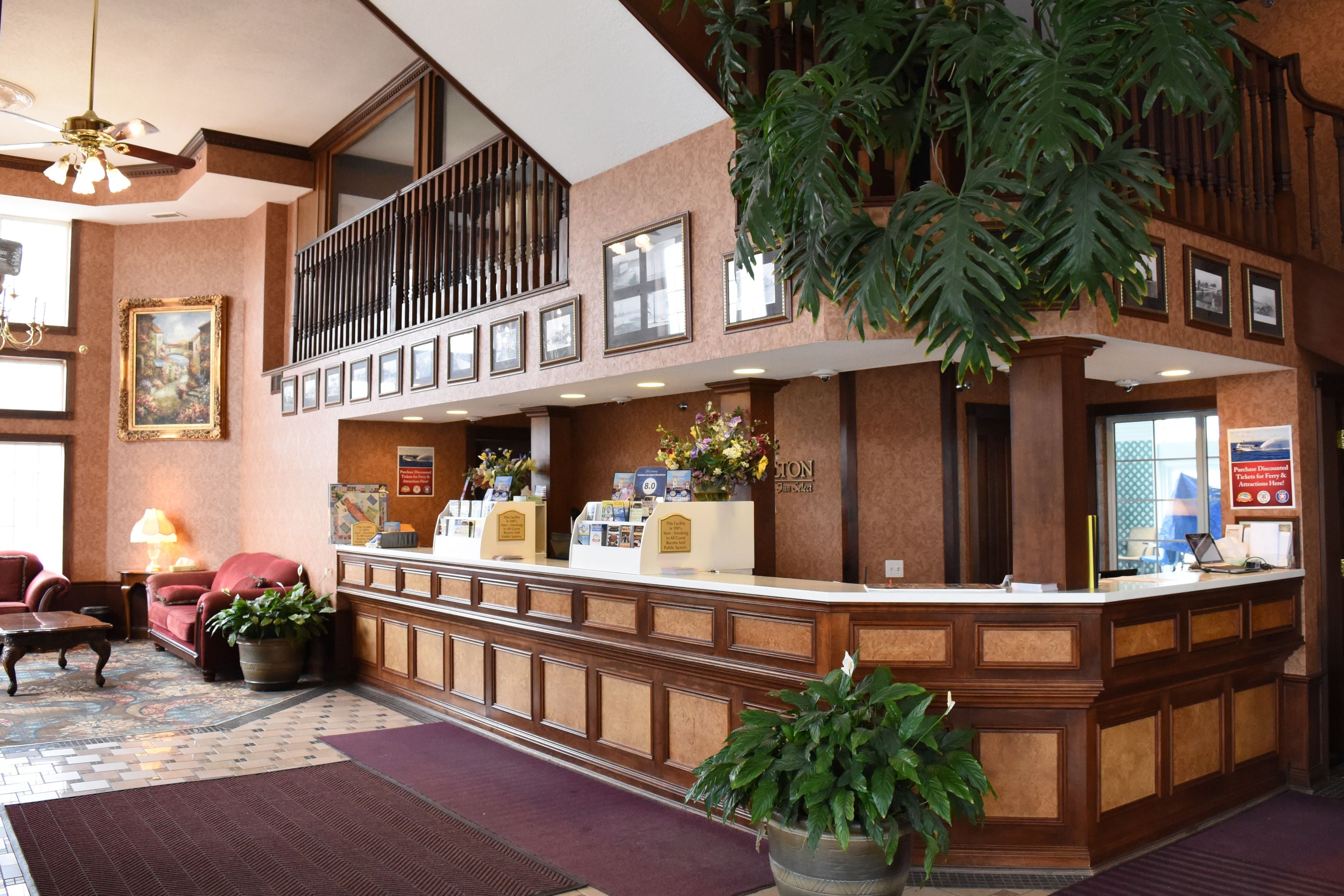 Zona de recepción de un hotel con un mostrador de madera, un área de descanso con sofá y sillones, una planta grande en maceta y un cuadro en la pared.
