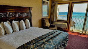 A hotel room with a large bed, a chair, and a view of the ocean through a sliding door. - Hamilton Inn Select Beachfront Mackinaw City (Mackinaw City)