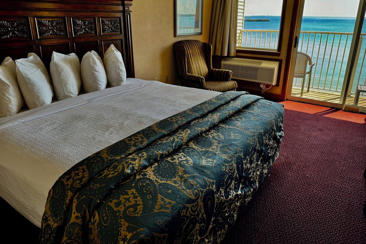 A hotel room with a large bed, a chair, and a view of the ocean through a sliding door.