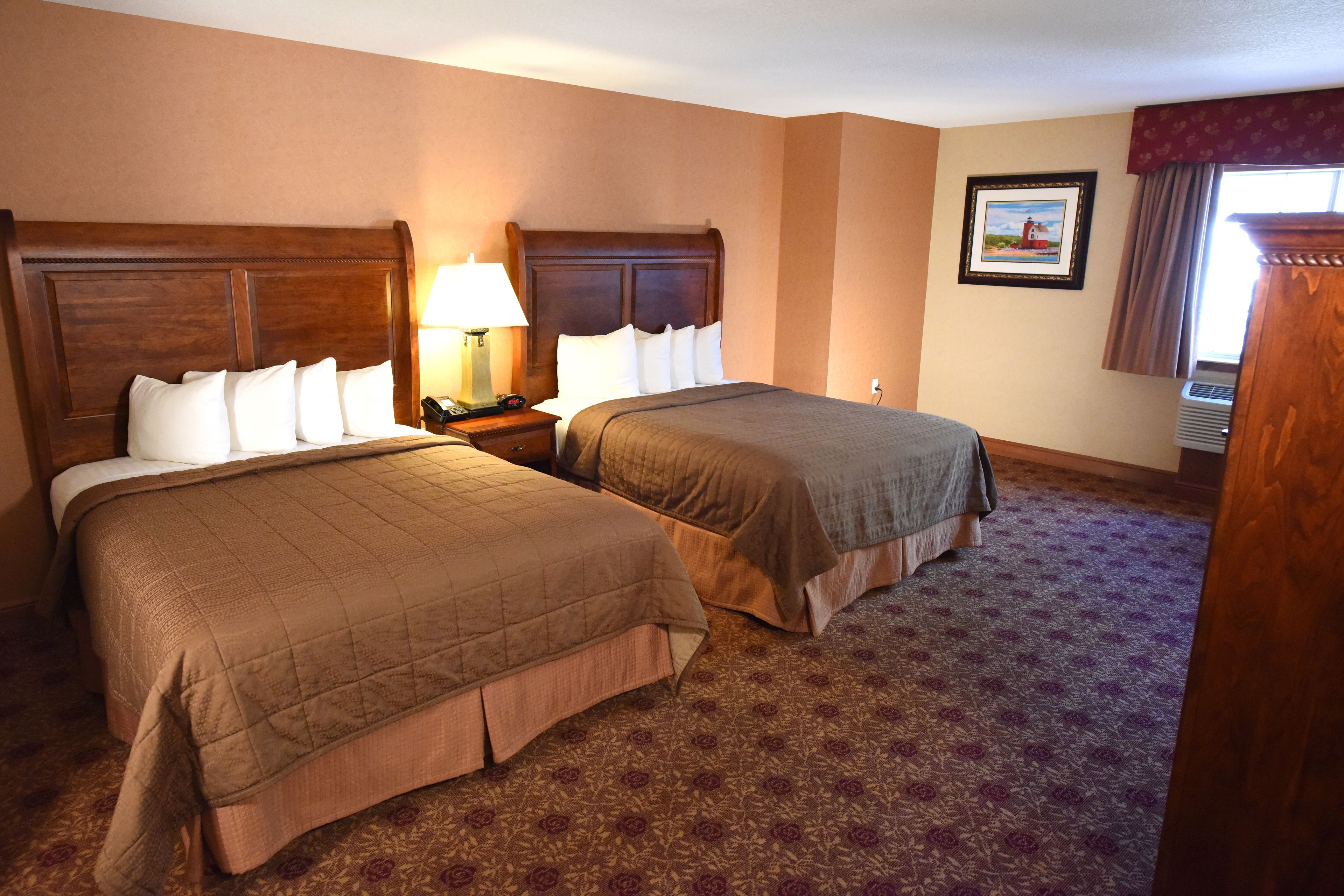 A hotel room with two beds, a nightstand with a lamp, a framed picture on the wall, and a window with curtains.