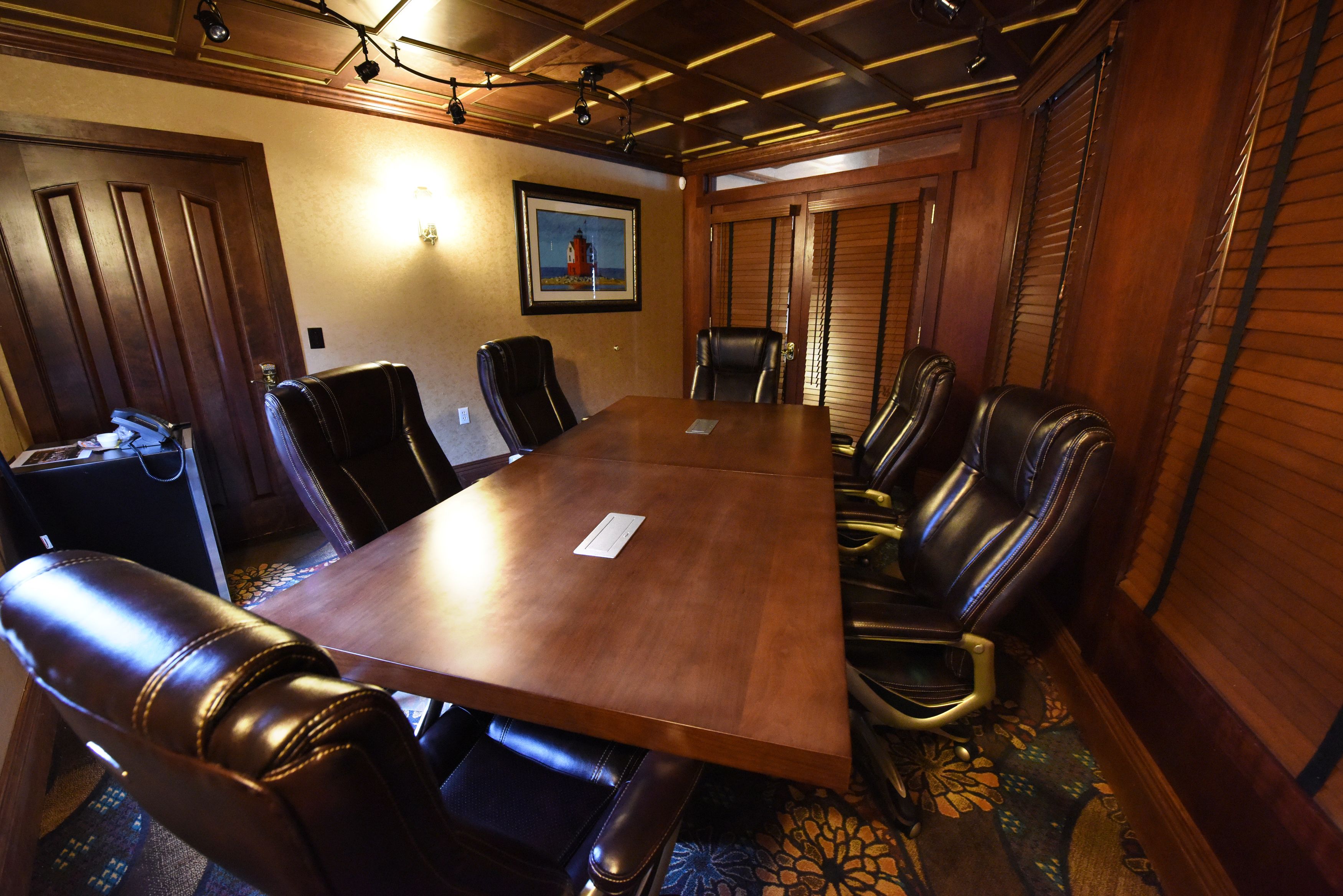 A conference room with a large wooden table, leather chairs, and a framed picture on the wall.