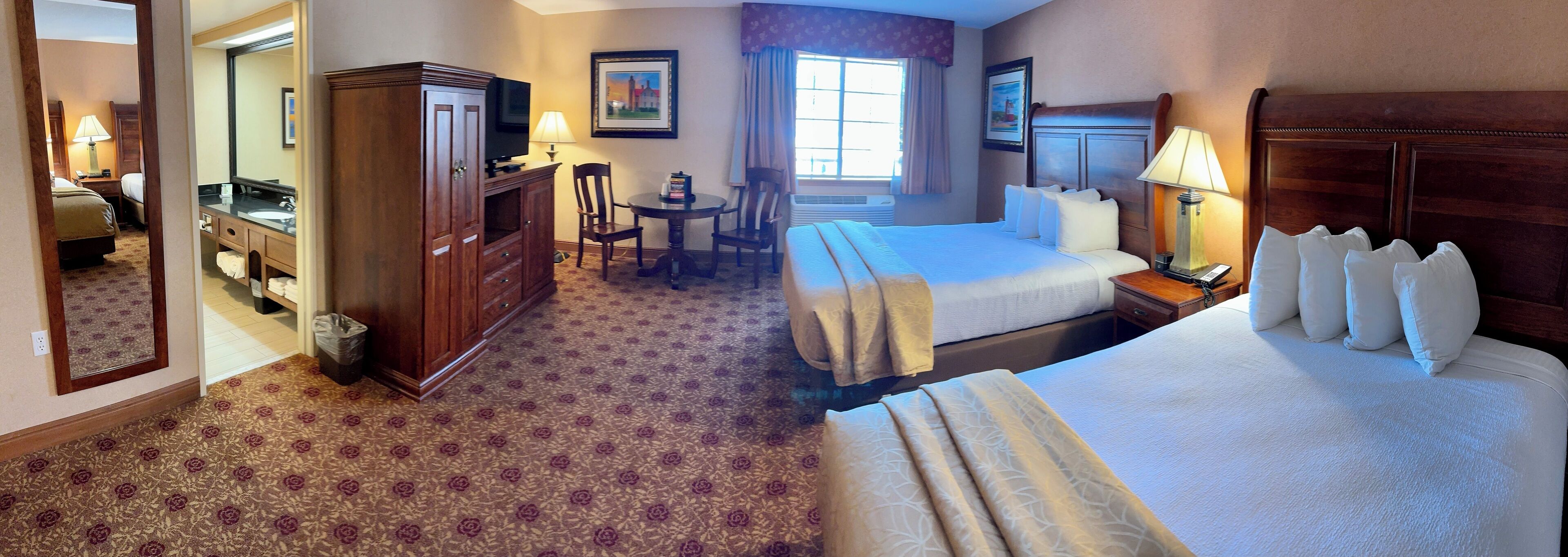 A hotel room with two beds, a desk, a chair, a TV, and a bathroom.