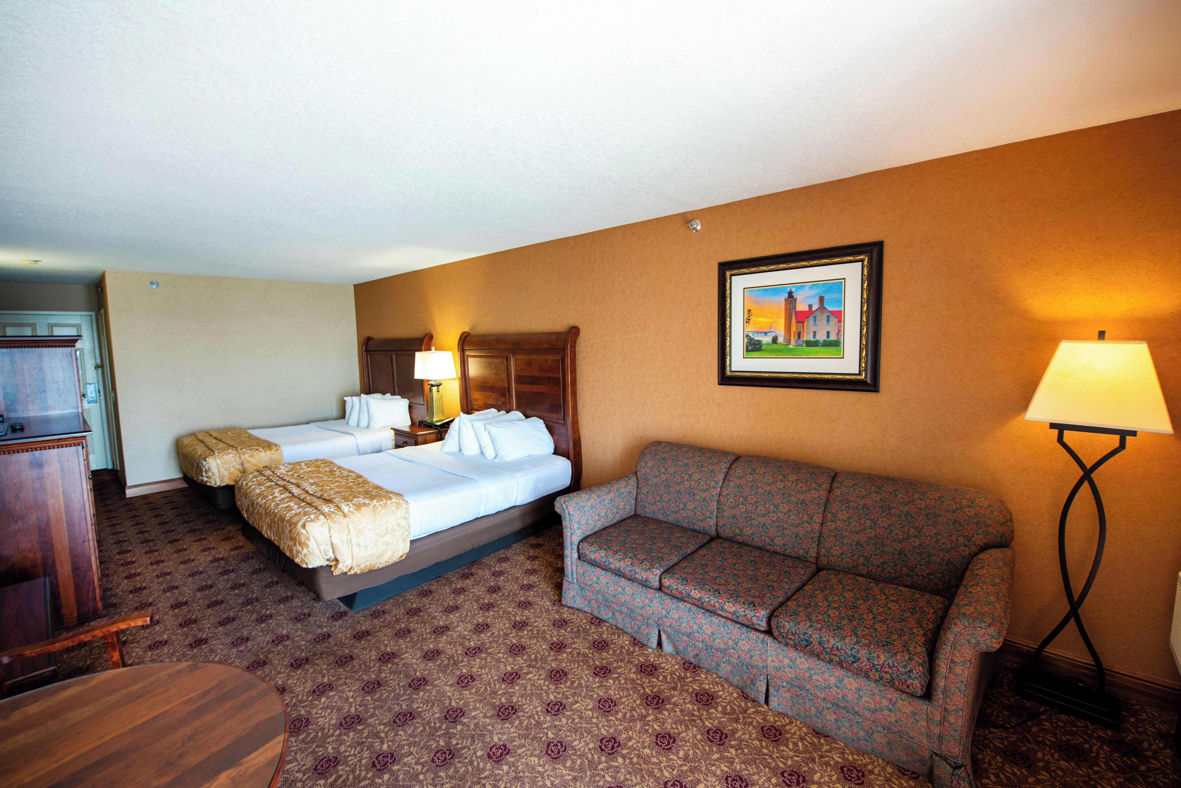 A hotel room with a bed, a sofa, a desk, and a lamp.
