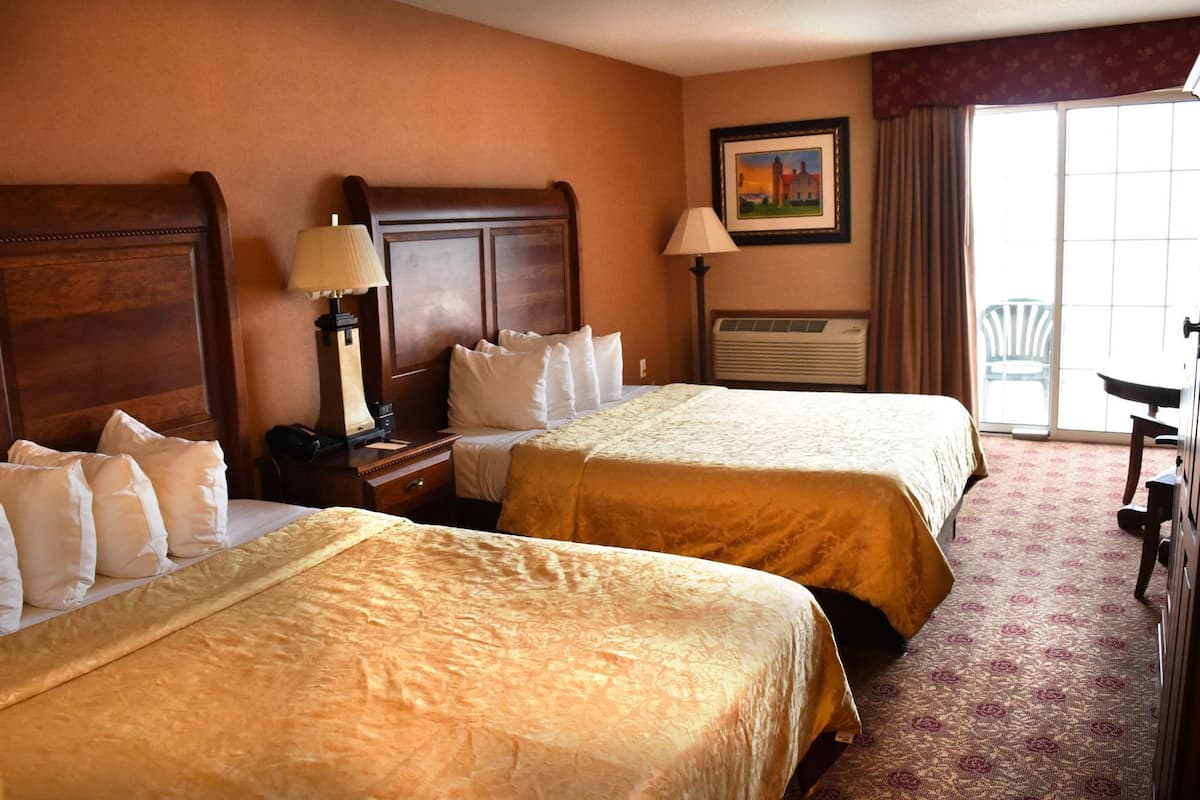 Une chambre d’hôtel avec deux lits, un bureau, une chaise, une lampe, un tableau et une fenêtre avec des rideaux.