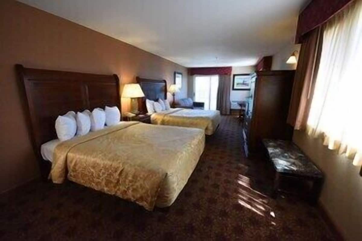 A hotel room with two beds, a bench, a desk, and a window.