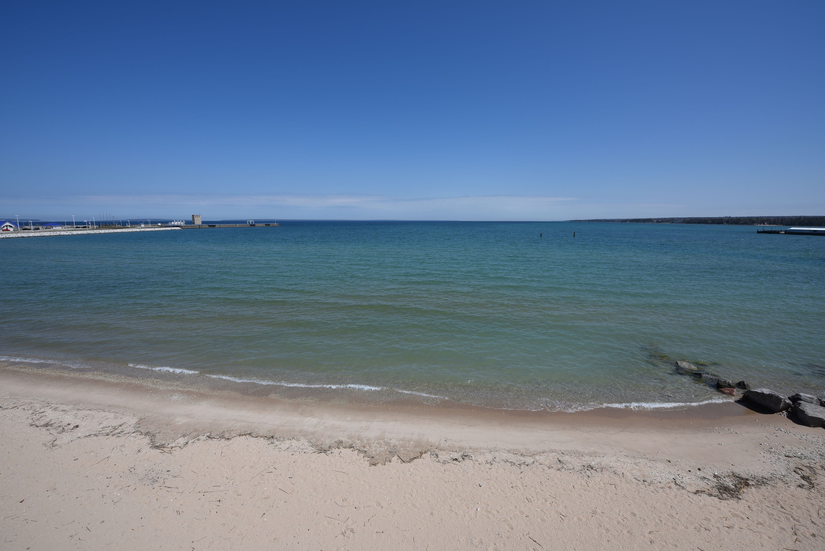 Una playa con aguas cristalinas, una orilla de arena y un muelle a lo lejos.