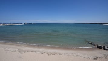 A beach with clear water, a sandy shore, and a distant pier.