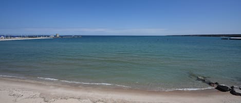 Una playa con aguas cristalinas, una orilla de arena y un muelle a lo lejos.