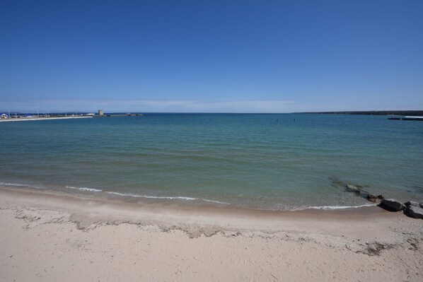 A beach with clear water, a sandy shore, and a distant pier.