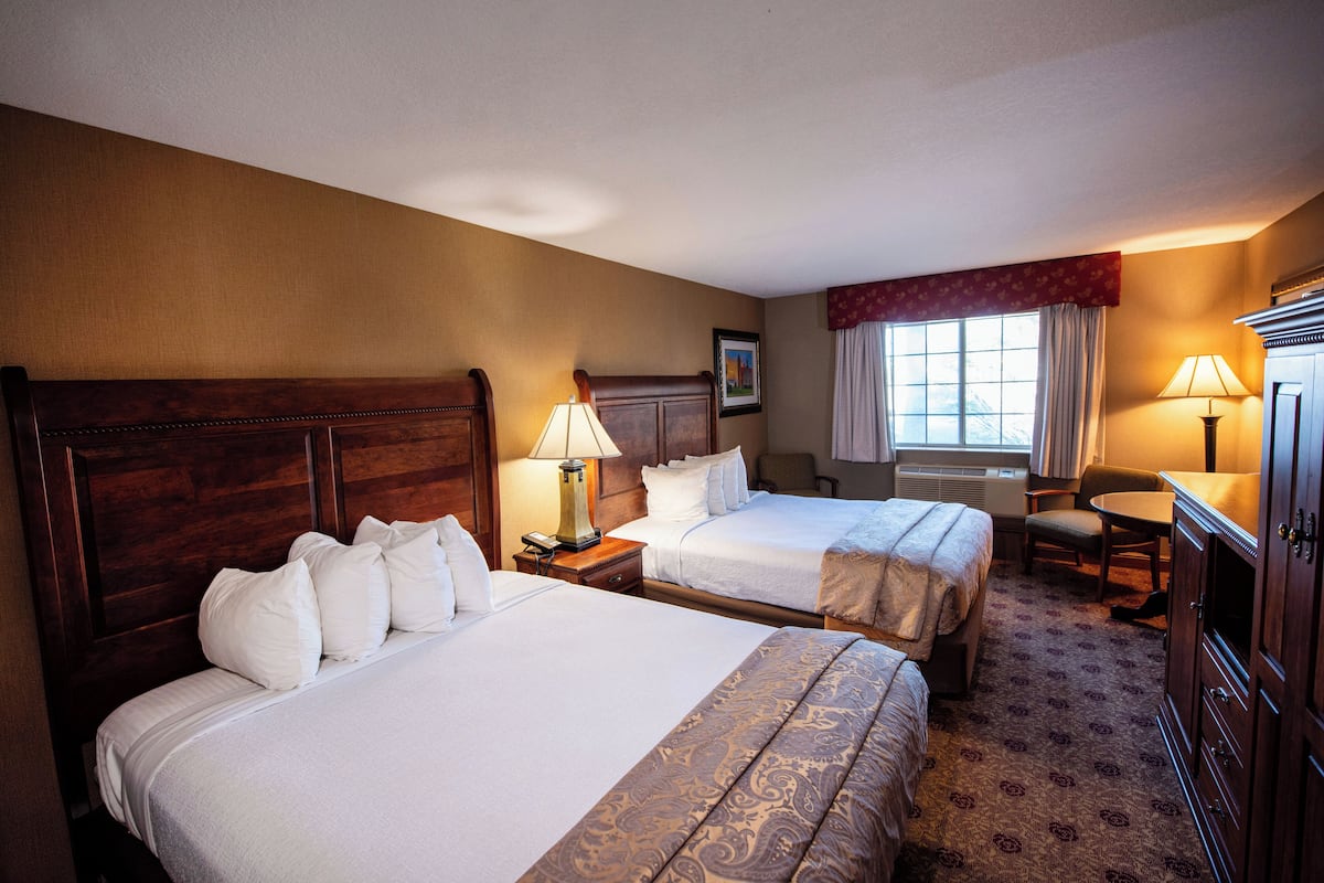 A hotel room with two beds, a desk, a chair, and a TV.