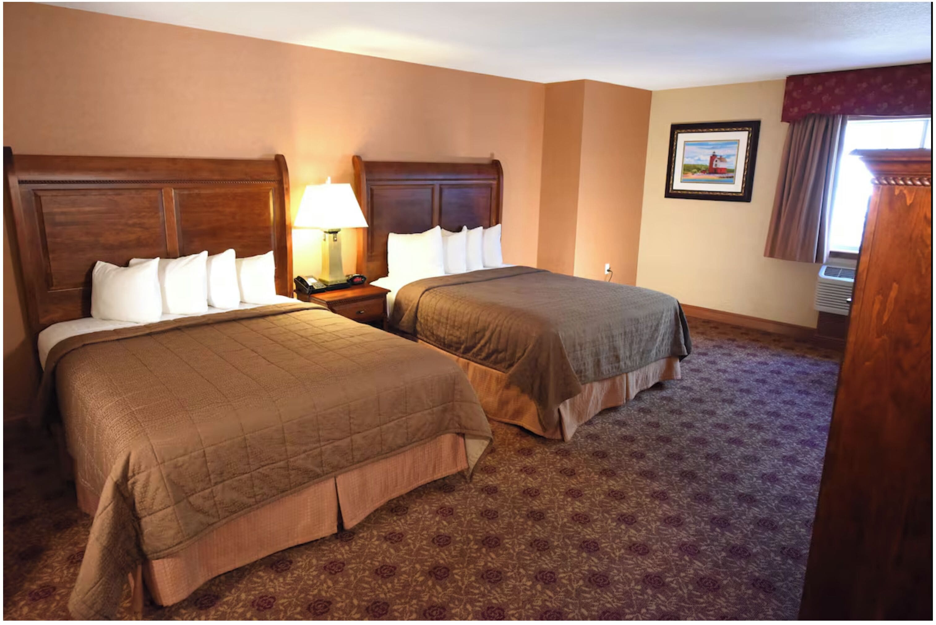 A hotel room with two beds, a nightstand with a lamp, a framed picture on the wall, and a window with curtains.