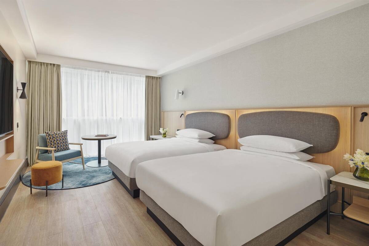 Une chambre d’hôtel avec deux lits, une télévision, une petite table, une chaise et une fenêtre avec des rideaux.
