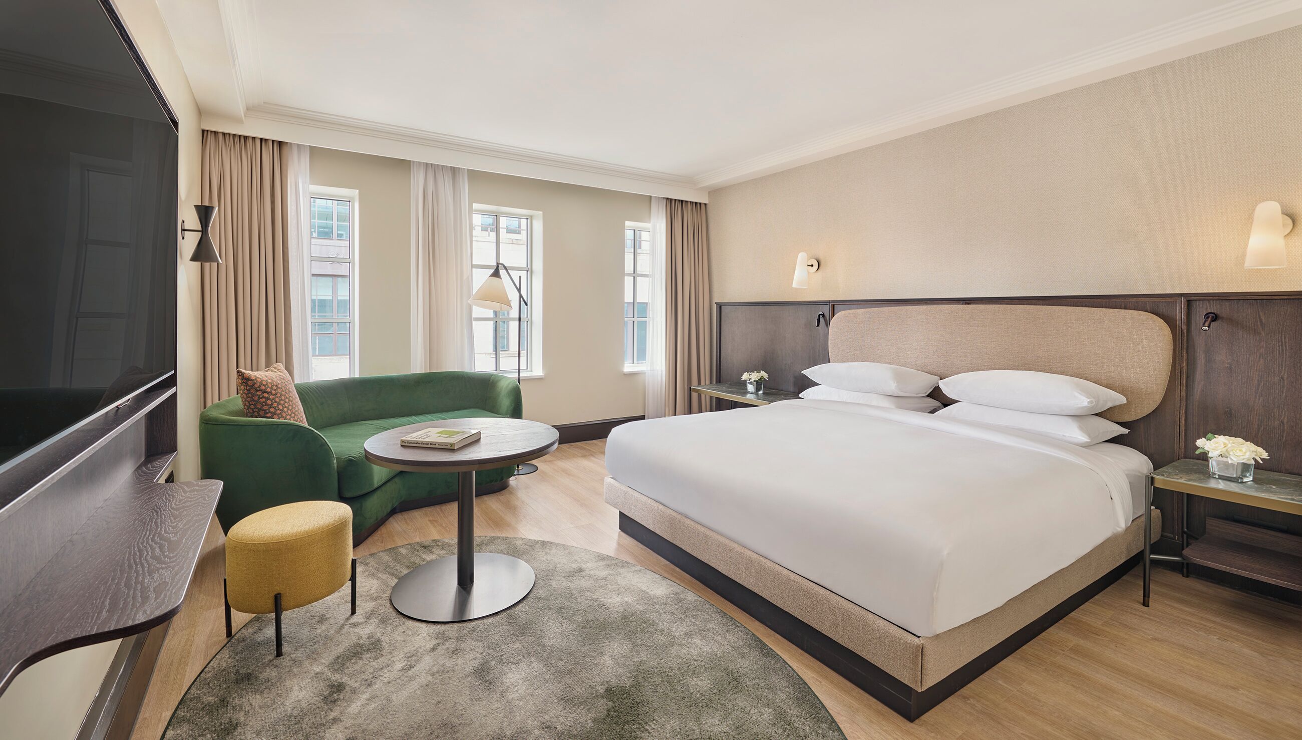 Une chambre d’hôtel avec un grand lit, un canapé vert, une petite table ronde, un téléviseur et une table de chevet avec une lampe.