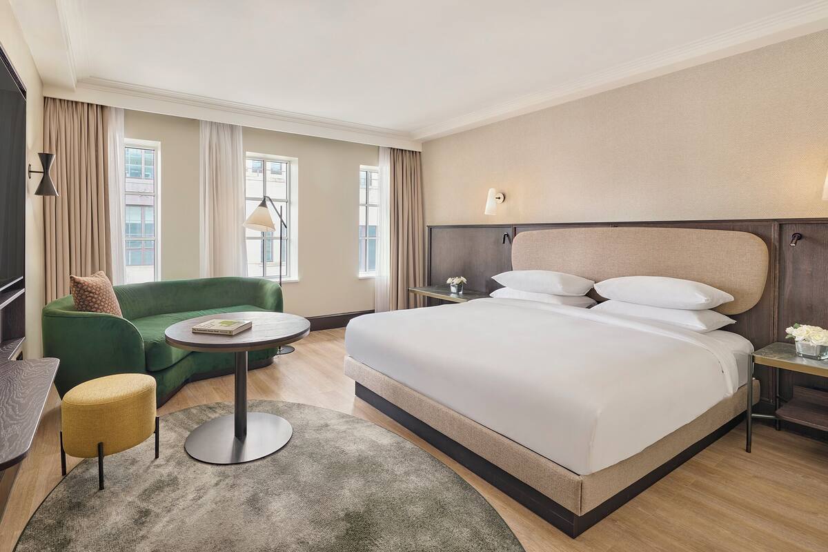 Une chambre d’hôtel avec un grand lit, un canapé vert, une petite table ronde, un téléviseur et une table de chevet avec une lampe.