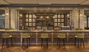 A bar area with a marble countertop, multiple stools, and a wine rack with bottles.