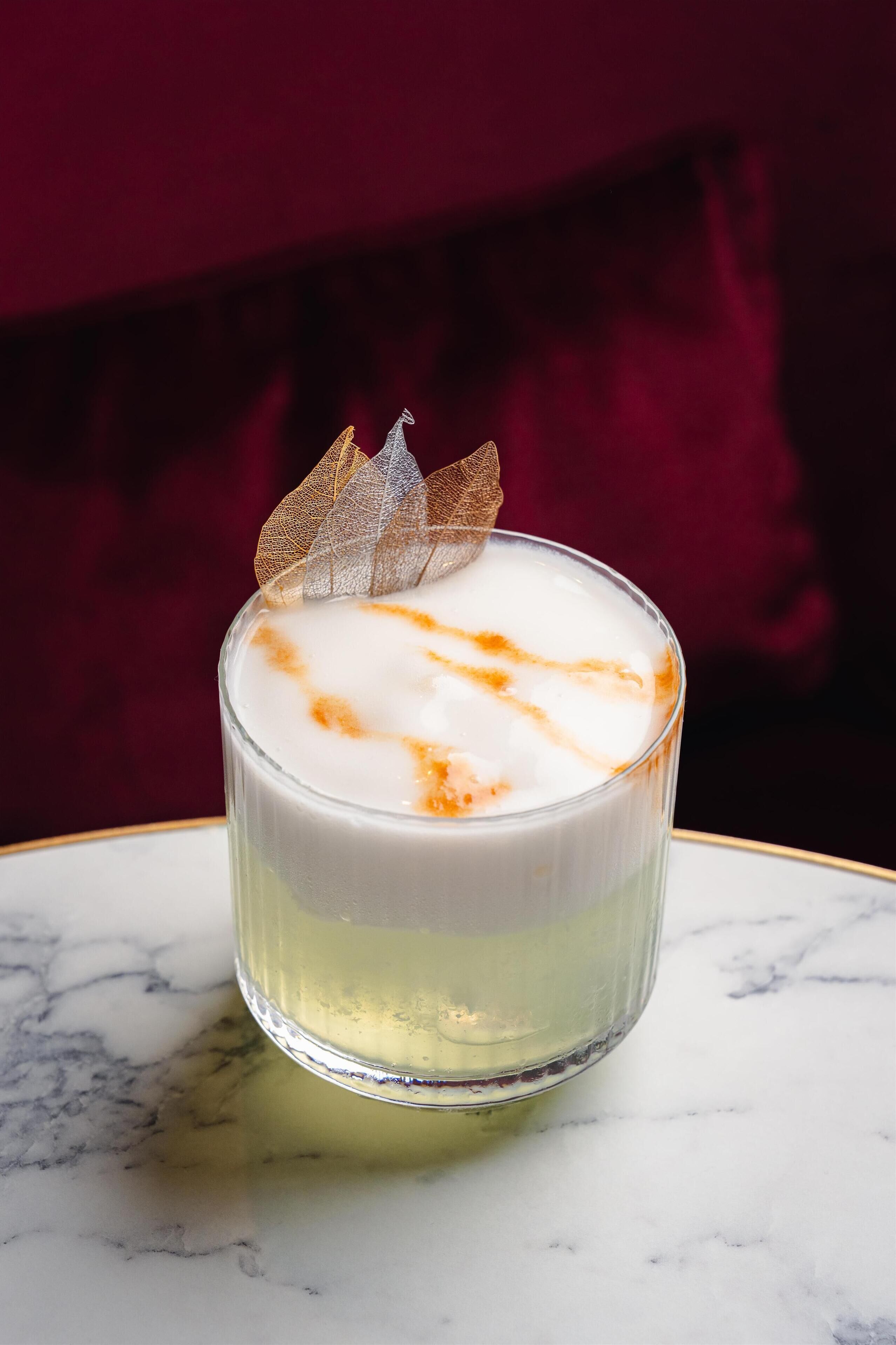 Un verre contenant une boisson crémeuse, orné d’une feuille décorative, posé sur une surface en marbre.
