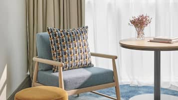 Een moderne kamer met een blauwe bank, een klein rond tafeltje met een bloevas, en een groot raam met dunne gordijnen.