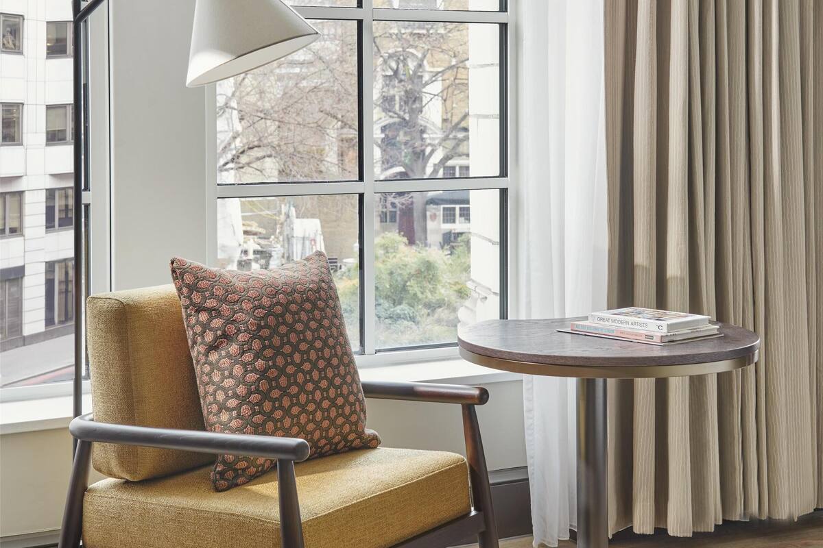 Une pièce avec une fenêtre, une chaise, une table et une lampe.