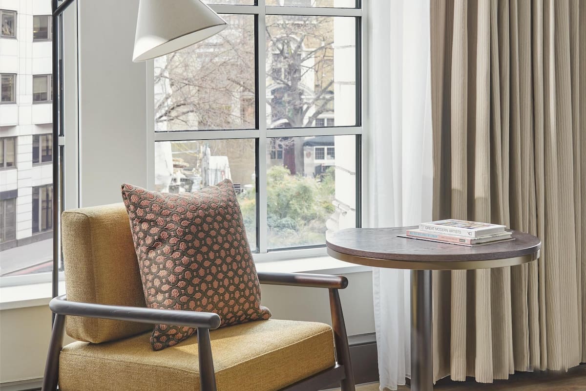 Una habitación con ventana, una silla, una mesa y una lámpara.