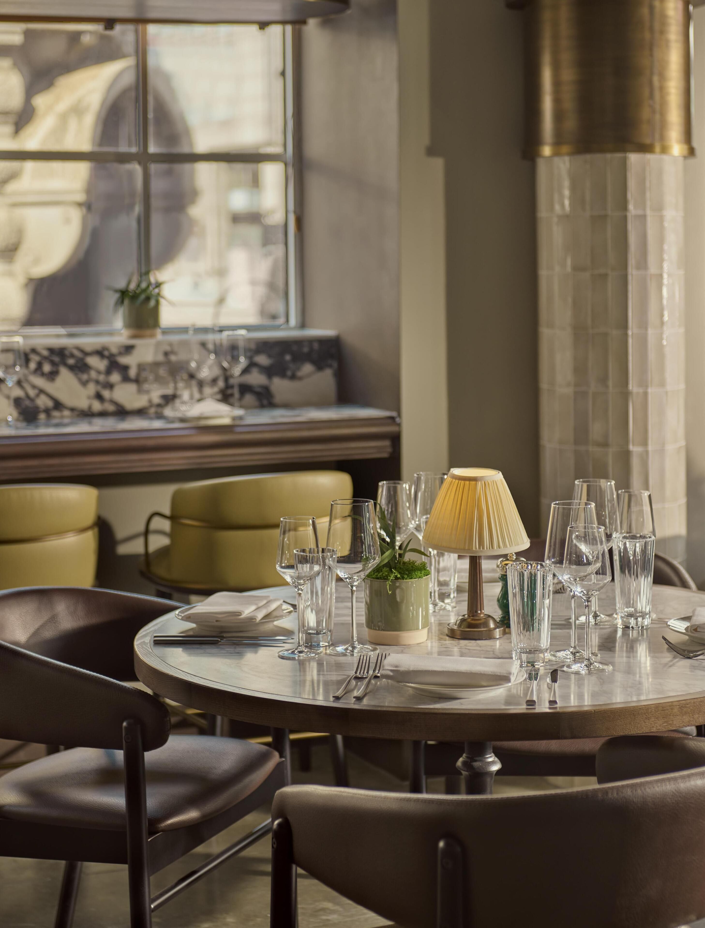 A round dining table with chairs, a lamp, and wine glasses.