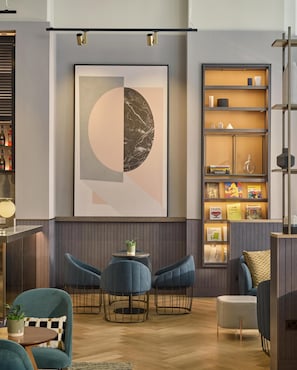 A modern interior with a large abstract painting, a bookshelf with books and decorative items, and a seating area with chairs and a table.