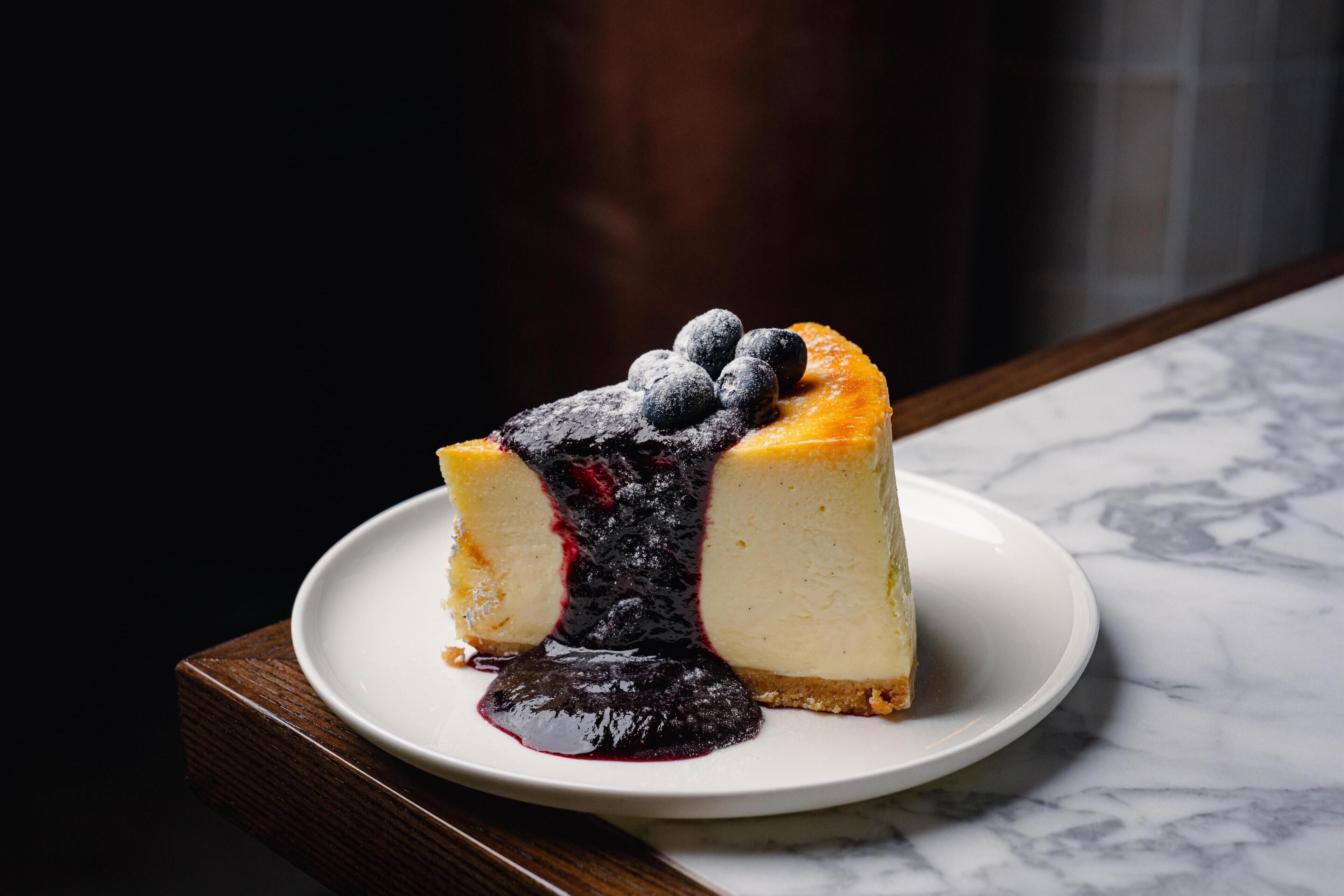 A slice of cheesecake with blueberries on a white plate on a marble surface.